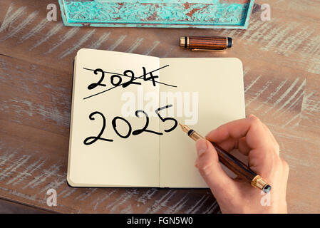 Retro-Effekt und getönten Bild einer Frau hand schreiben eine Notiz mit einem Füllfederhalter auf einem Notebook. Motivations-Konzept mit handschriftlichen Text Happy New Year 2025 und 2024 abgeschrieben Stockfoto