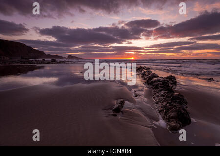 Sonnenuntergang am Welcombe Mund Beach in North Devon, UK. Es gibt einen schönen orangefarbenen Himmel, unberührten Sand und schöne Wolken. Stockfoto