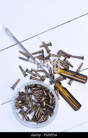 Box mit Messingschrauben und Schraubendreher auf Holztisch Stockfoto