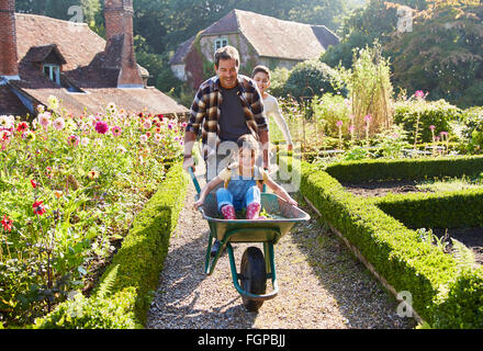 Vater schob Tochter in Schubkarre im sonnigen Garten Stockfoto