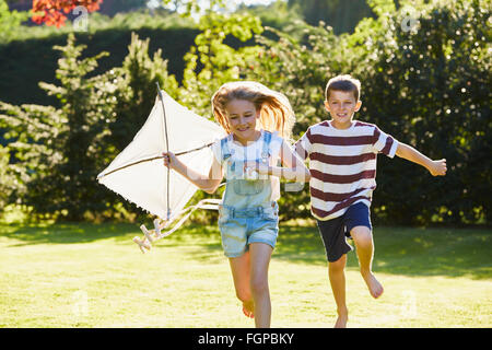 Bruder und Schwester laufen mit Drachen im sonnigen Garten Stockfoto