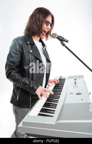 Profil von charismatischer junger Mann mit langen Haaren spielen auf Synthesizer und Gesang Mikrofon auf weißem Hintergrund Stockfoto