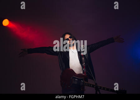 Berühmte junge männliche Sänger über bunte rauchigen Hintergrund mit e-Gitarre und Mikrofon auf der Bühne stehen Stockfoto