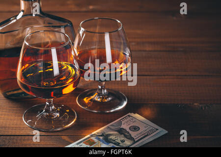 Zwei Gläser cognac und Flasche, mit Bündel Geld auf den Tisch. Stockfoto