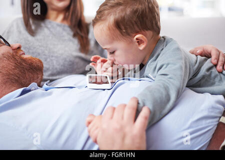 Neugierig Kleinkind Blick auf Handy an des Vaters Brust Stockfoto