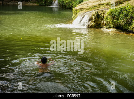 Landschaft mit kleinen Wasserfall durch den See und eine Person schwimmen an einem Sommertag Stockfoto