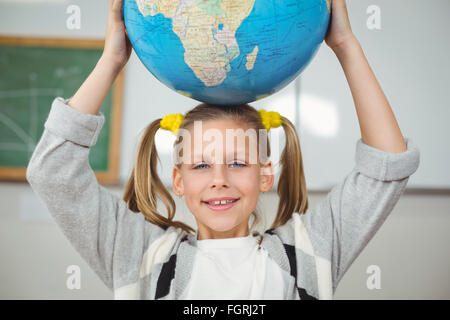 Nette Schüler balancieren Globus auf Kopf in einem Klassenzimmer Stockfoto