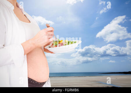 Zusammengesetztes Bild des Mittelteils des schwangeren mit Salat Stockfoto