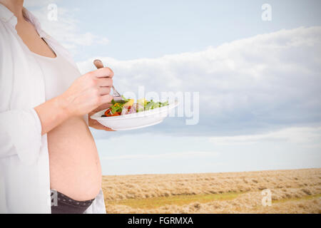 Zusammengesetztes Bild des Mittelteils des schwangeren mit Salat Stockfoto