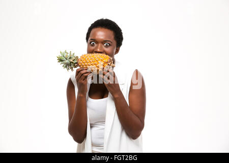 Hungrigen aufgeregt afroamerikanischen jungen Frau halten und beißen frischen Ananas auf weißem Hintergrund Stockfoto