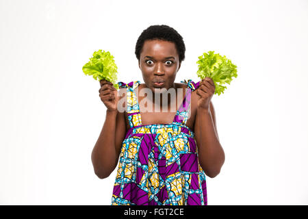Lustig aufgeregt afroamerikanischen jungen Frau im bunten Sommerkleid mit Salatblätter auf weißem Hintergrund Stockfoto