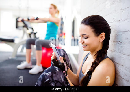 Fit Woman in Turnhalle hält Smartphone, Mauer Stockfoto