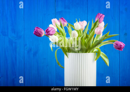Vase mit weißen, rosa und lila Tulpen vor blau bemalten Holzwand Stockfoto