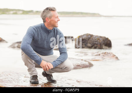 Mann kauerte auf einem großen Felsen Stockfoto