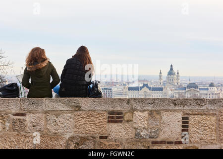 BUDAPEST, Ungarn - 02. Februar: Zwei Mädchen sitzen auf Wand, genießen die Aussicht vom Burgpalast mit Gresham Palace und Saint-Ste Stockfoto