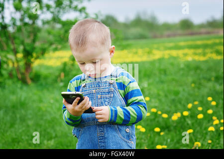 kleiner Junge Blick auf einem Smartphone auf einer Wiese Stockfoto