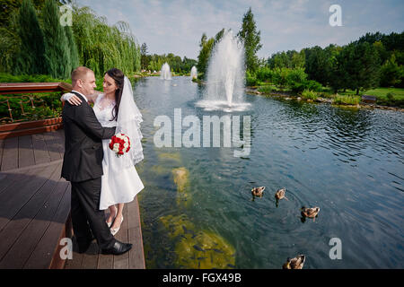 elegante stilvolle Bräutigam mit seiner glücklich wunderschöne Braut auf dem Hintergrund eines Sees mit Enten