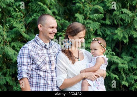 glückliche Familie mit einer kleinen Tochter auf einem Hintergrund aus grünen Blättern Stockfoto