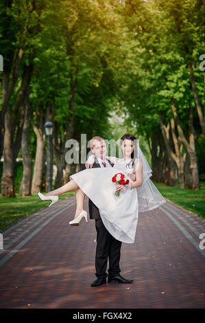 Bräutigam hält seine Braut in den Armen und einem Lächeln des Glücks im Sommerpark Stockfoto