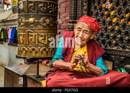 Sehr alte tibetische buddhistische Nonne sitzt und bittet vor einem Heiligtum in Kathmandu Stockfoto