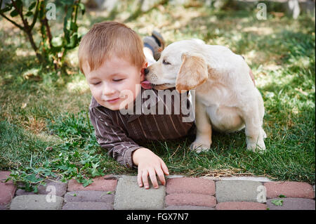 kleiner Junge spielt mit einem weißen Labrador-Welpe Stockfoto