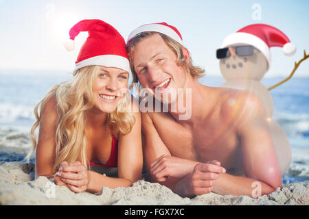 Zusammengesetztes Bild des Paares liegen am Strand tragen Weihnachtsmützen Stockfoto
