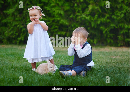 kleiner Junge mit dem Mädchen und Kaninchen spielen auf der Wiese Stockfoto