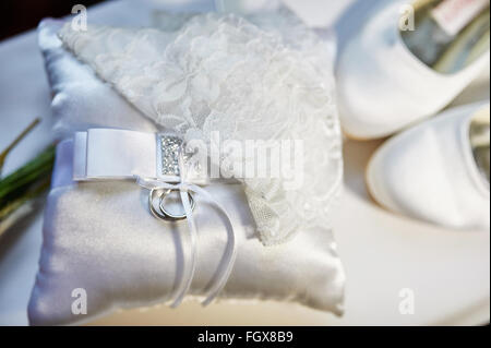 Trauringe auf einem Kissen und die Braut weiße Schuhe Stockfoto