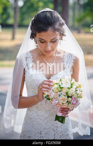 Braut in einem weißen Kleid im grünen Sommerpark mit einem Blumenstrauß in der hand Stockfoto