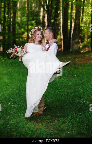 Junge Bräutigam trägt seine schöne Frau im park Stockfoto