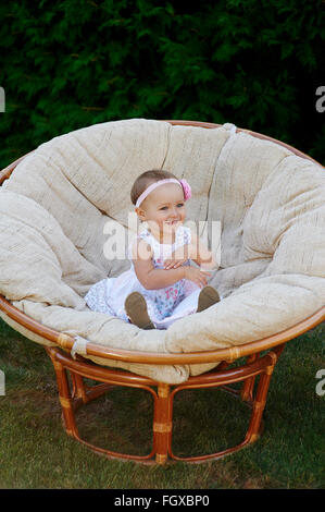 Kleines Mädchen posiert auf einem weißen Stuhl.  Sie lächelt glücklich Stockfoto