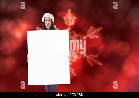 Zusammengesetztes Bild glücklich Brünette in Nikolausmütze zeigt weißes Plakat Stockfoto
