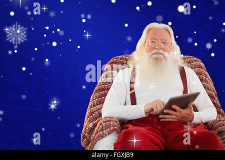 Zusammengesetztes Bild des Lächelns Santa mit Tablet auf dem Sessel Stockfoto