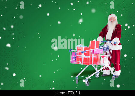 Zusammengesetztes Bild von Santa schiebt einen Einkaufswagen mit Geschenken Stockfoto