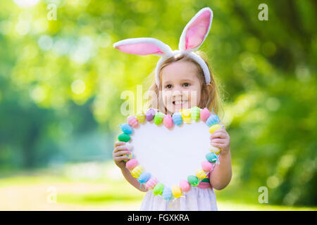 Kleines Mädchen Spaß auf Ostereiersuche. Kinder in Hasenohren und Hase Kostüm. Kinder mit bunten Eiern in einem Korb. Stockfoto