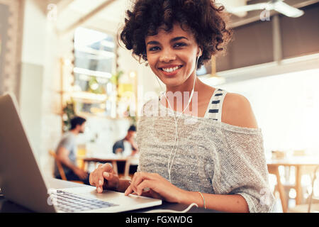 Porträt der glückliche junge afrikanische Frau mit einem Laptop im Café. Lächelnde Frau in Coffee-Shop mit einem Laptop sitzt. Stockfoto