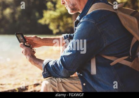 Porträt von reifer Mann sitzt an einem See mit einem Kompass für die Navigation zugeschnitten. Wanderer-Mann Suche Richtung mit einem Kompass ou Stockfoto