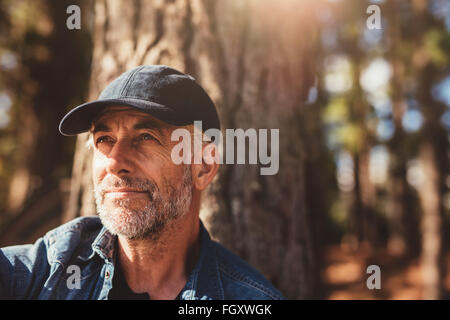 Porträt von senior Mann mit Mütze wegsehen hautnah. Reifer Mann mit Bart im Wald an einem Sommertag sitzen. Stockfoto