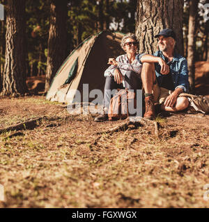Porträt von glücklich älteres paar beisammen sitzen unter einem Baum im Wald. Ältere Mann und Frau entspannend auf ihrem Campingplatz. Stockfoto