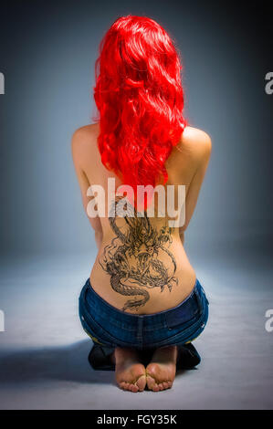 Junge Dame mit einem Drachen Tattoo und rote Haare auf Boden sitzend zurück Stockfoto