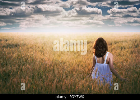 Frau starrte auf einen dramatischen Himmel in einem goldenen Feld. Abendlicht Stockfoto