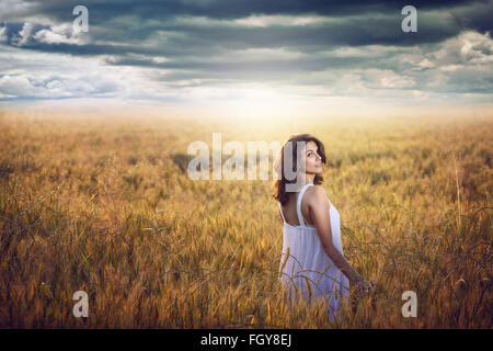 Schöne Frau in einem Kornfeld mit dramatischen Himmel. Abendlicht Stockfoto