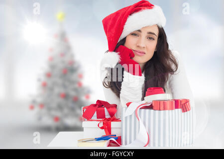 Zusammengesetztes Bild unsicher Brünette in Nikolausmütze Verpacken Geschenke Stockfoto