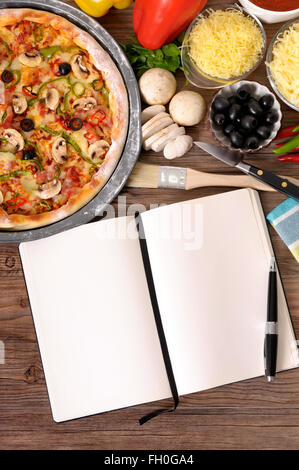 Frisch gebackene Pizza mit leeren Notebook oder Kochbuch umgeben von verschiedenen Zutaten. Stockfoto