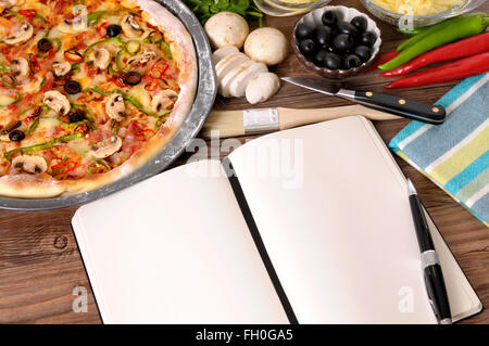 Frisch gebackene Pizza mit leeren Notebook oder Kochbuch umgeben von verschiedenen Zutaten. Stockfoto