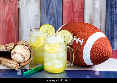 Glas Gläser gefüllt mit kalte Limonade mit sportlichen Elementen.  Holztafeln gemalt, rot, weiß und blau im Hintergrund verblasst. Stockfoto