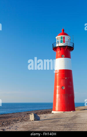 Ein rot-weißen Leuchtturm auf dem Meer unter strahlend blauem Himmel. Fotografiert in der Nähe von Westkapelle in Zeeland, Niederlande. Stockfoto