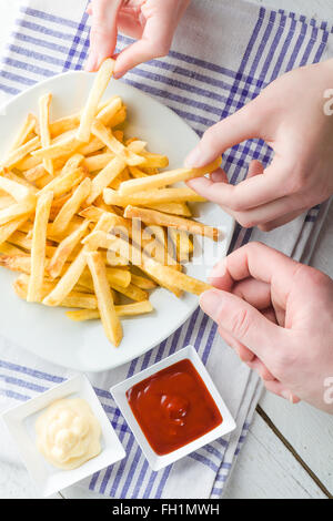 Drei Hände Kommissionierung Pommes Frites mit Ketchup und Mayonnaise Stockfoto