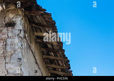 Beschädigtes Dach eines alten Hauses, von unten gesehen mit blauen Himmel im Hintergrund Stockfoto