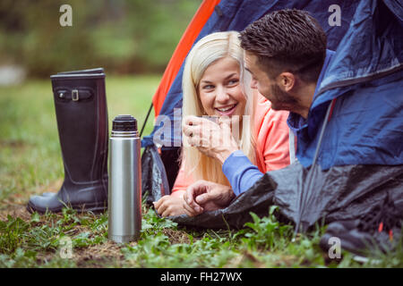 Glückliches Paar liegen im Zelt mit heißen Getränken Stockfoto